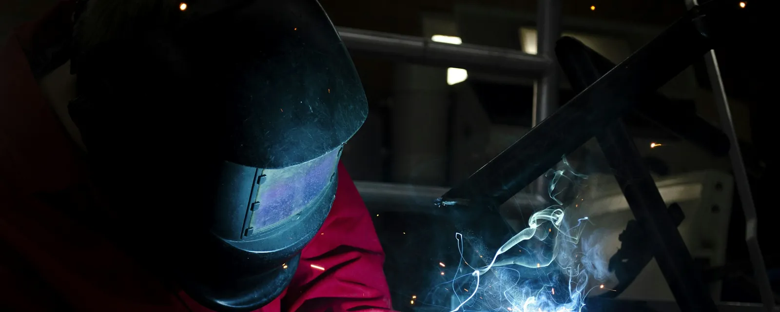 A bright blue welding arc and sparks under a welder's helmet in a dark shop